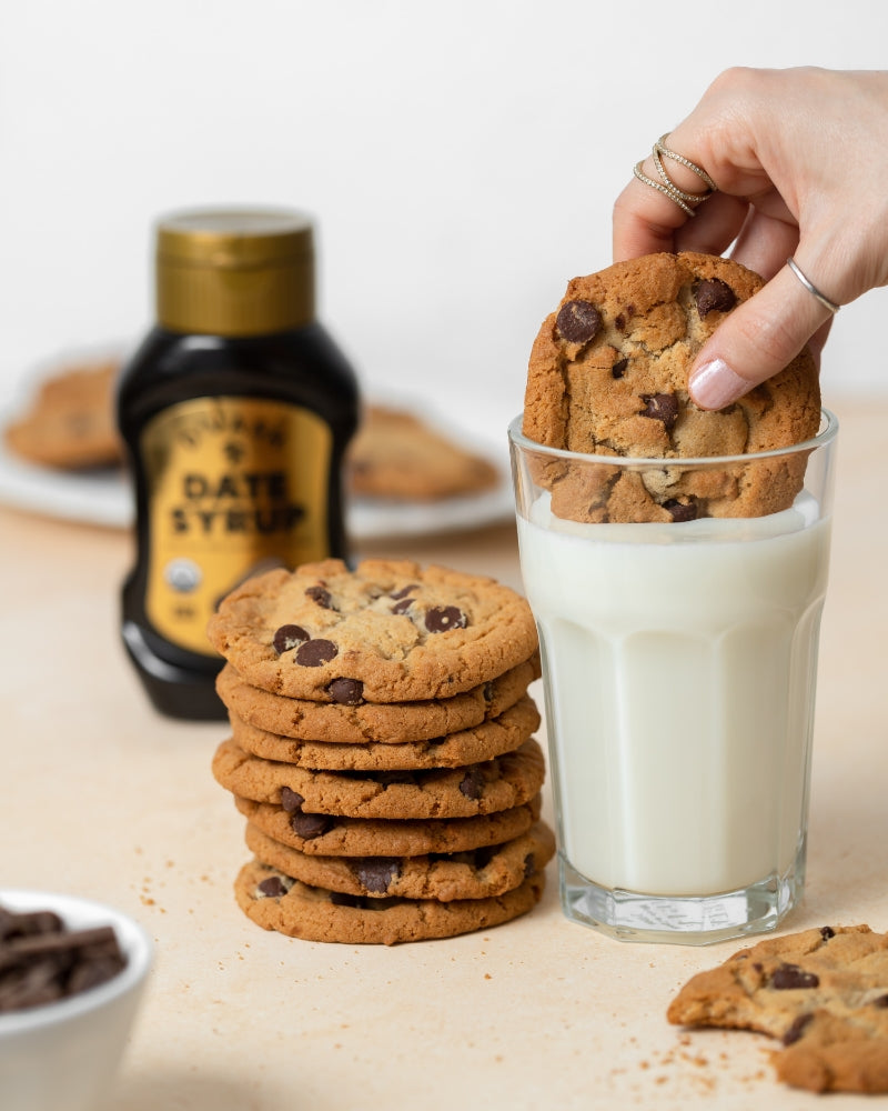 chocolate chip cookies dunked into milk. organic date syrup bottle in background